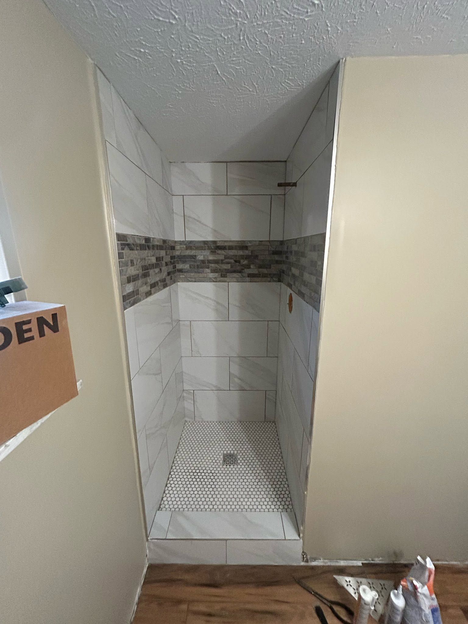 Empty tiled shower stall with a narrow built-in shelf and mosaic accent band.