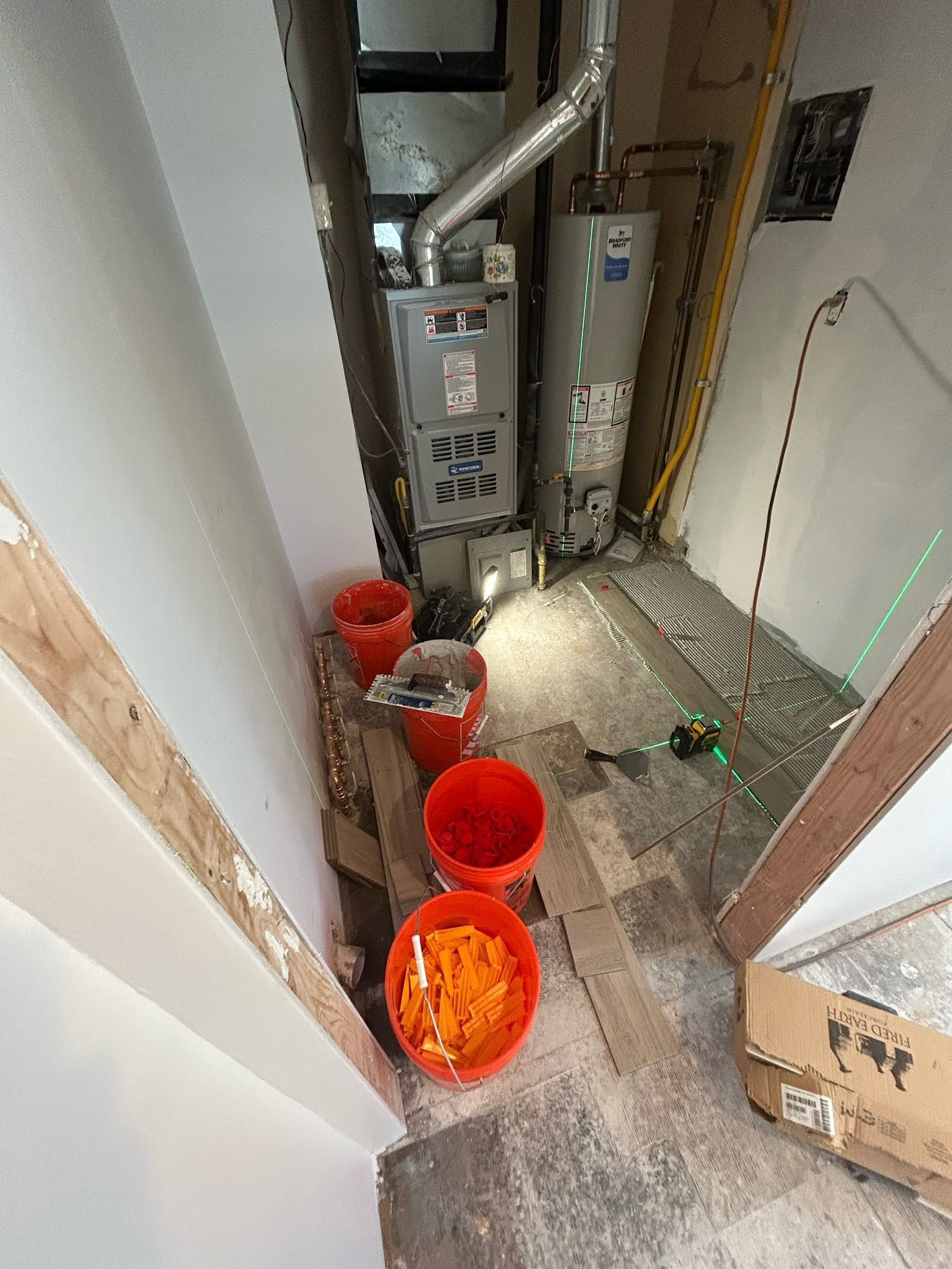 Narrow utility room with furnace and ductwork, cluttered floor, and several orange buckets.