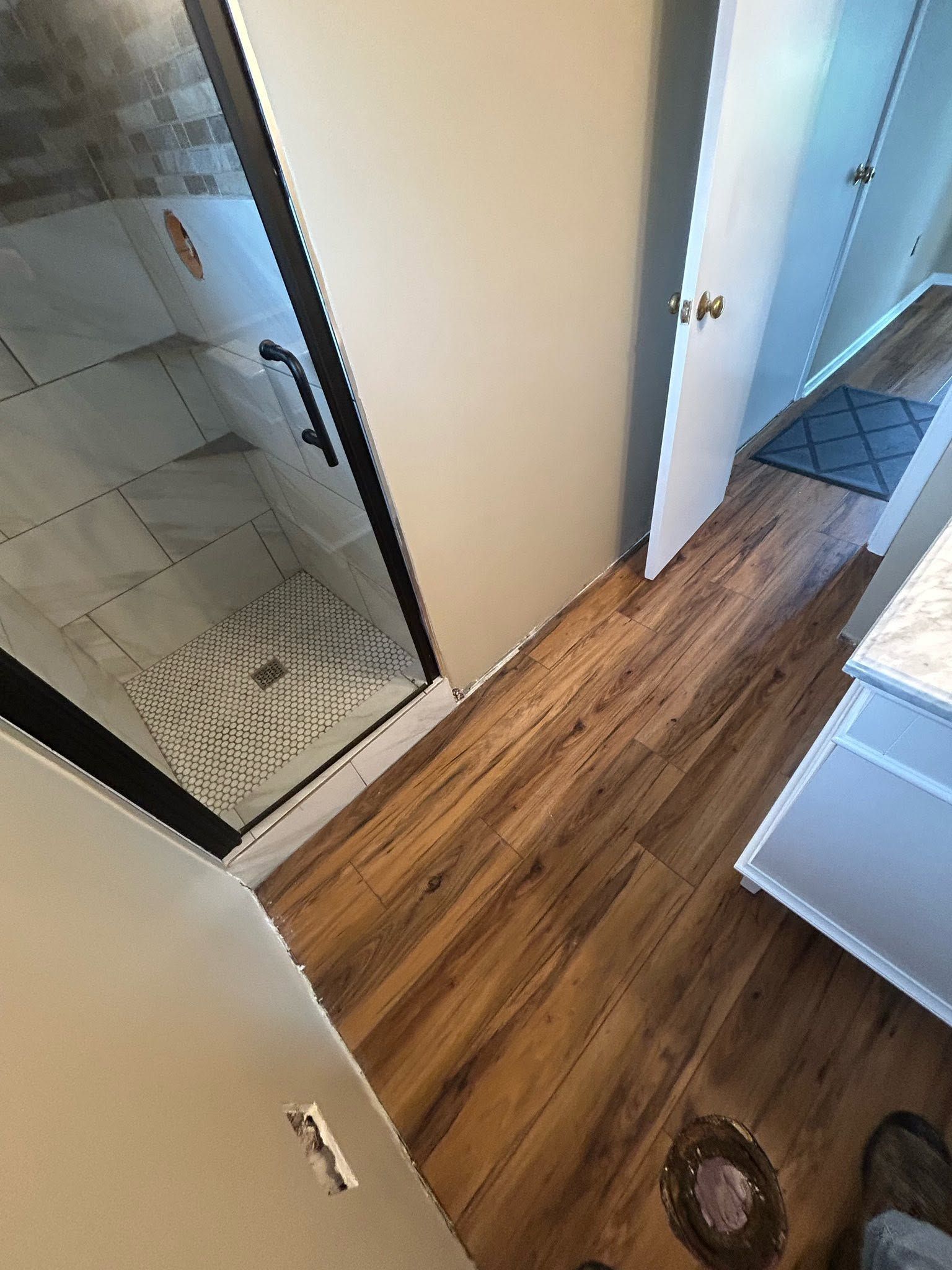 Hallway with wood floor, mirror closet door, white walls, and a doorway to a tiled bathroom.