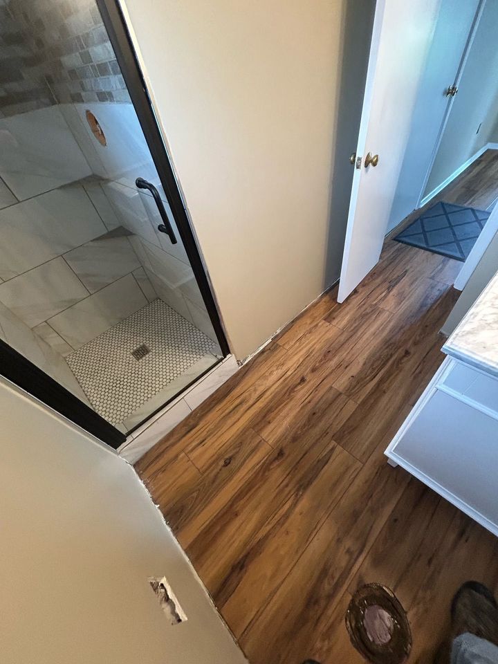 Hallway with wood floors, bathroom tiles on left, open doors, and a white dresser on the right
