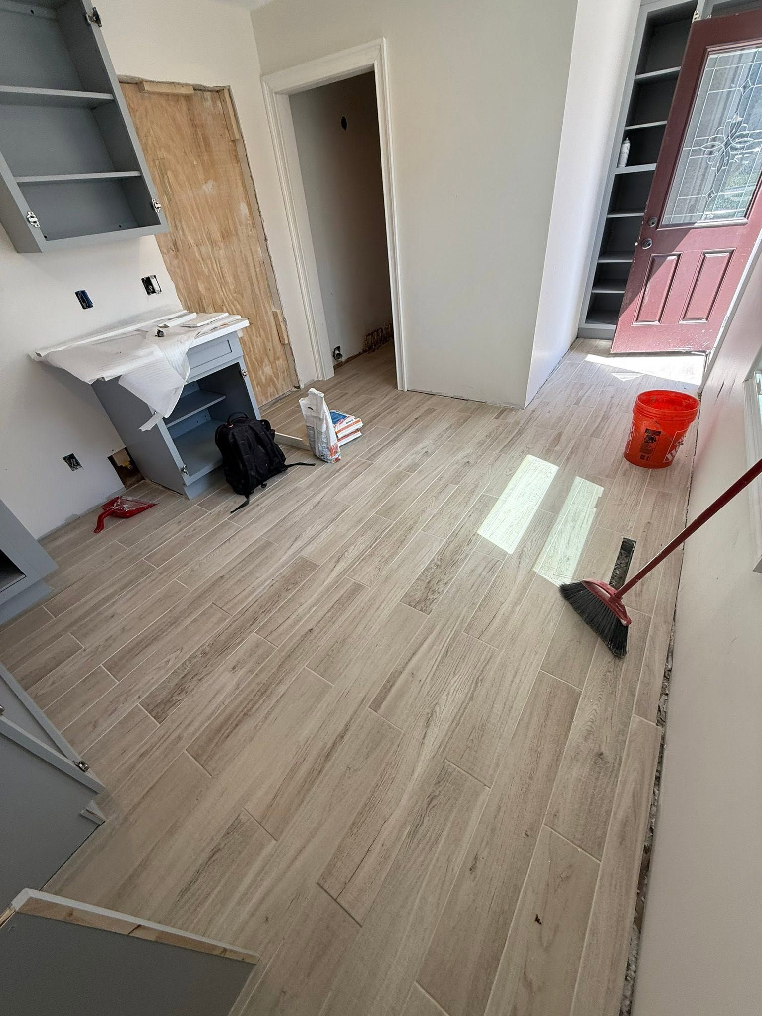 Partially renovated room with tiled floor, sink, open door, shelving, and cleaning tools near a window
