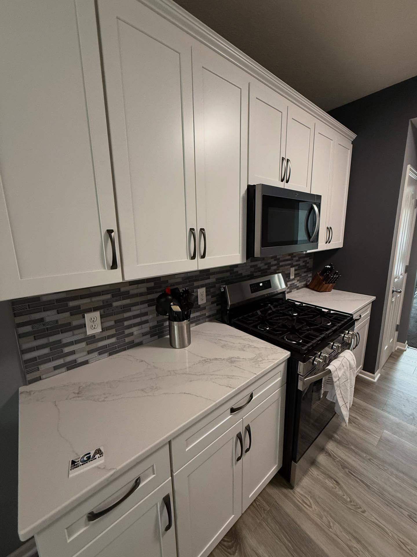 Modern white kitchen with marble counters, stainless stove and microwave, gray tile backsplash, and wood floors