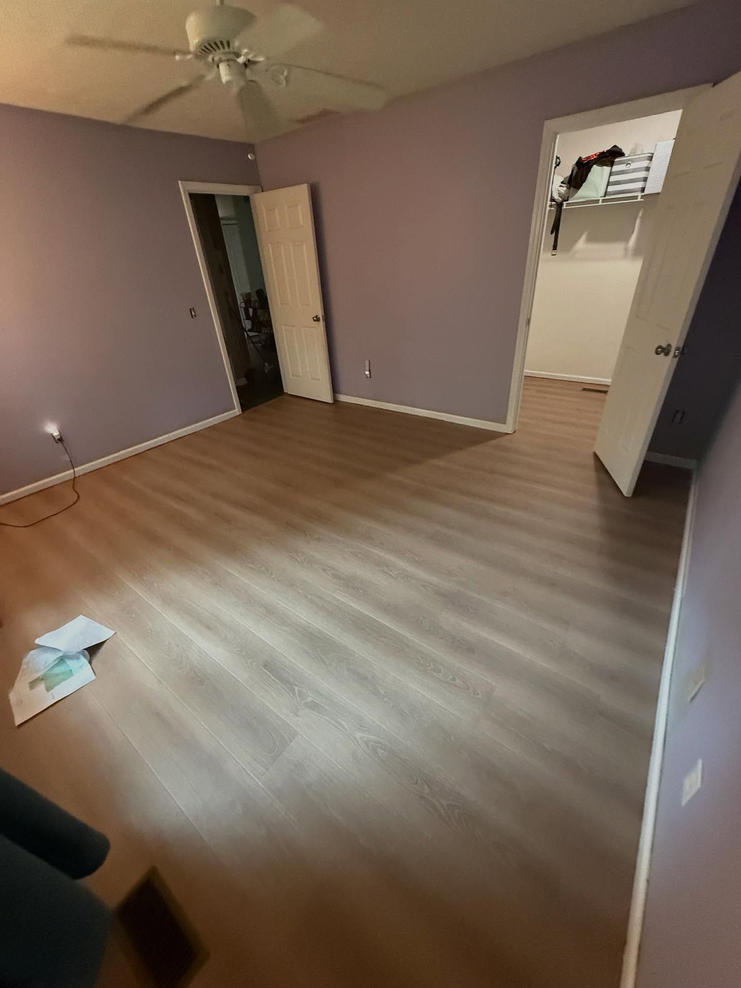 Empty purple bedroom with wood-pattern floor, open closet, ceiling fan, and open door to hallway