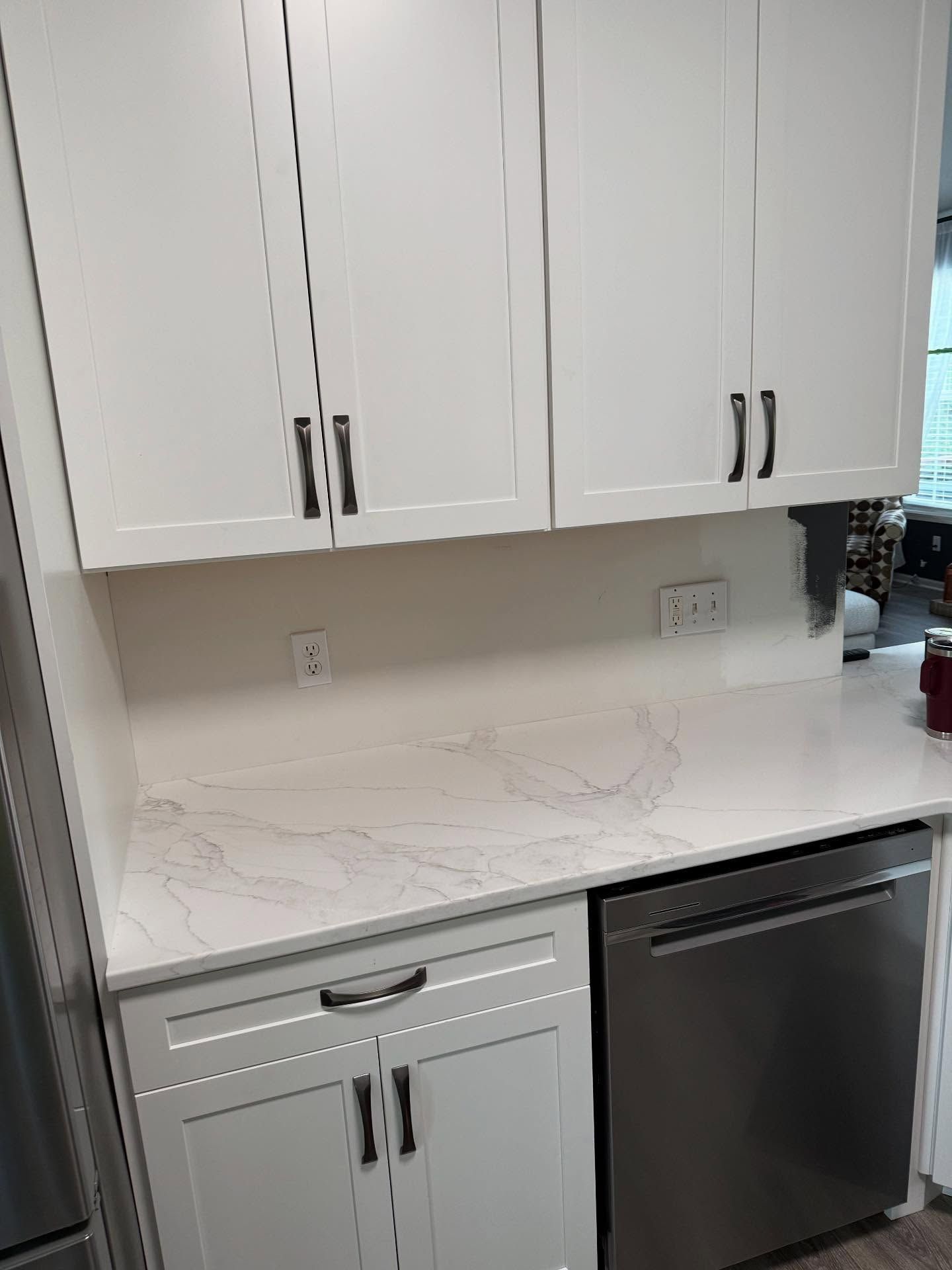 White kitchen cabinets and marble-look countertop with a black dishwasher underneath.