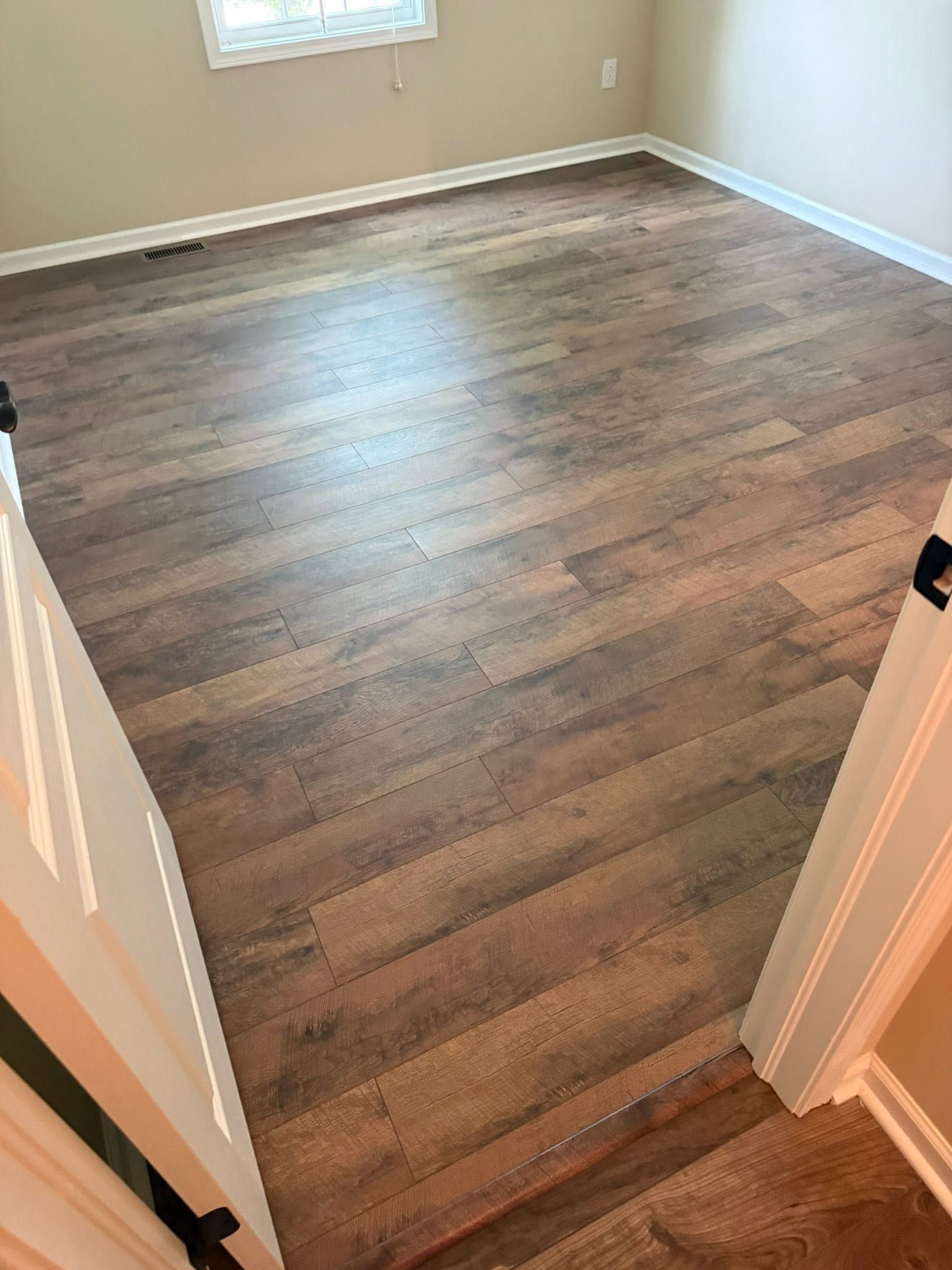Empty room with wood-look flooring, beige walls, and a window letting in daylight.