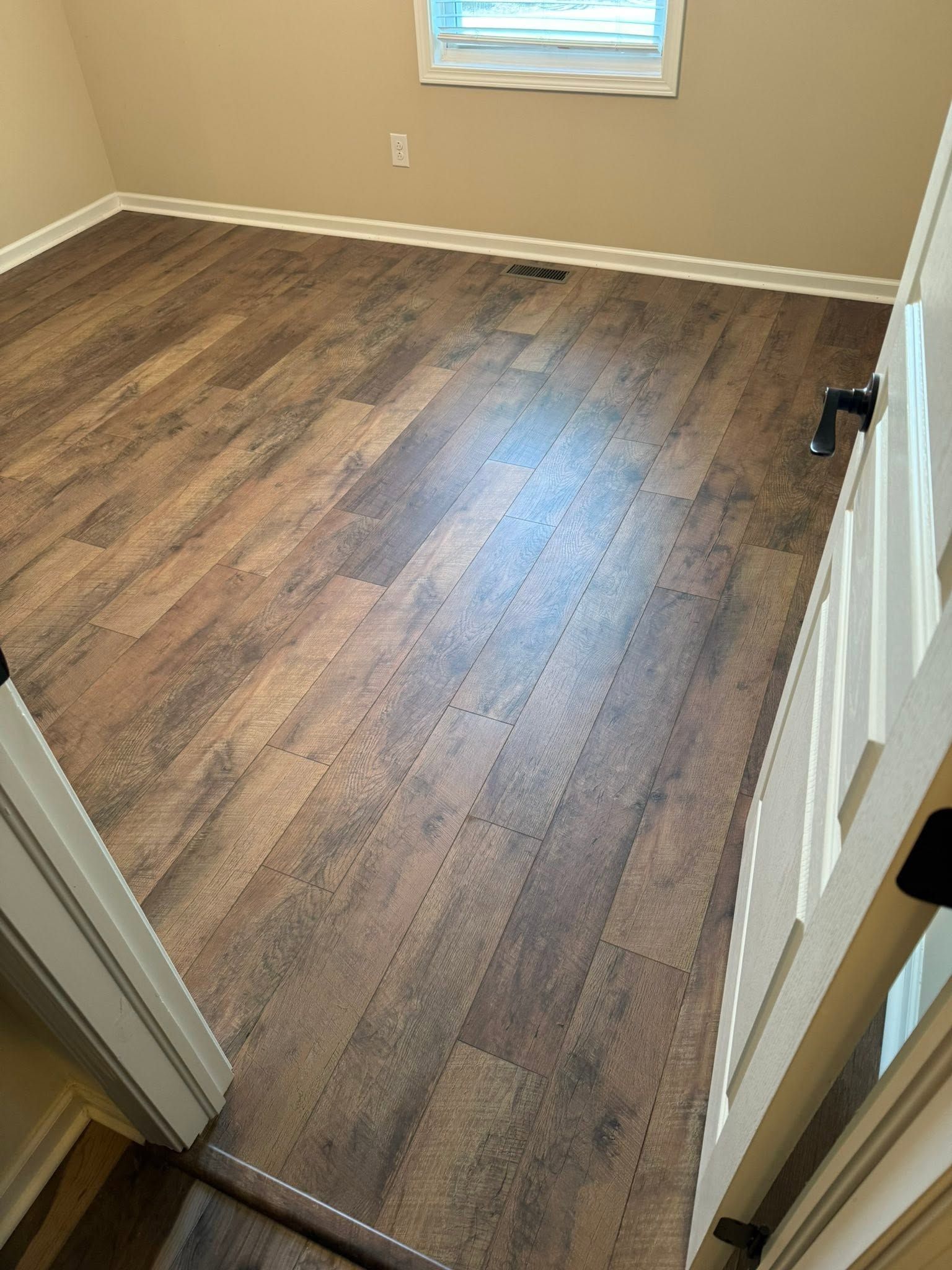 Empty beige room with wood-look flooring and a small window, viewed from a doorway.