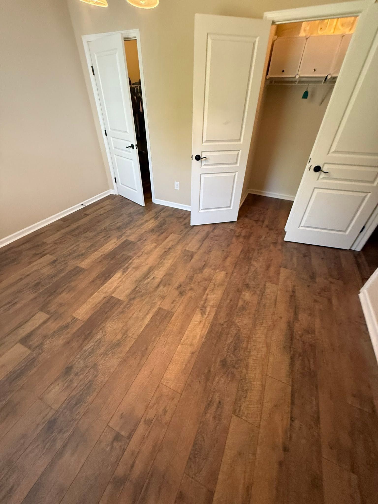 Empty bedroom with wood-look flooring and open closet doors.