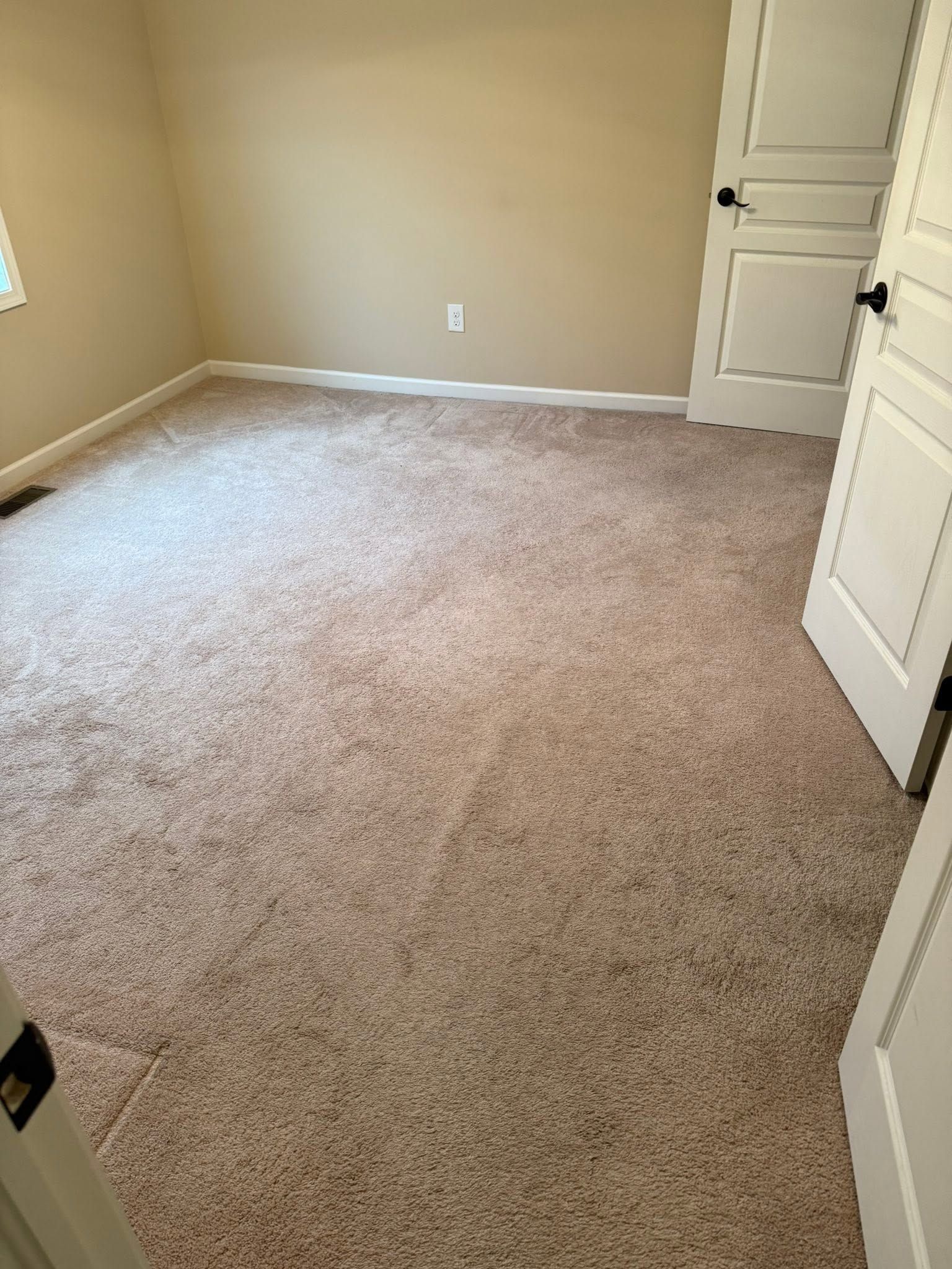 Empty beige carpeted room with open white door and light walls