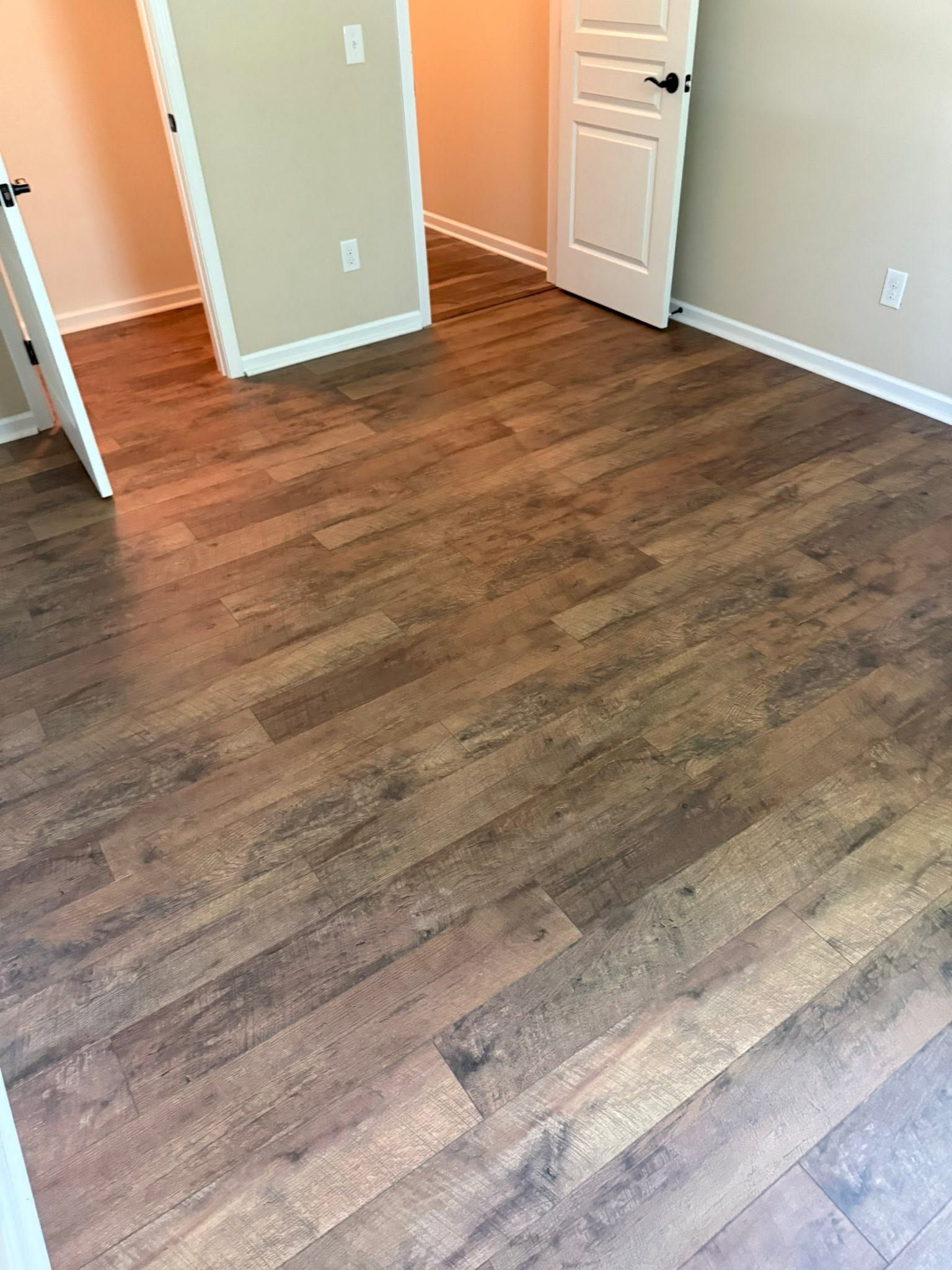 Empty room with wood-look flooring, beige walls, and an open white door
