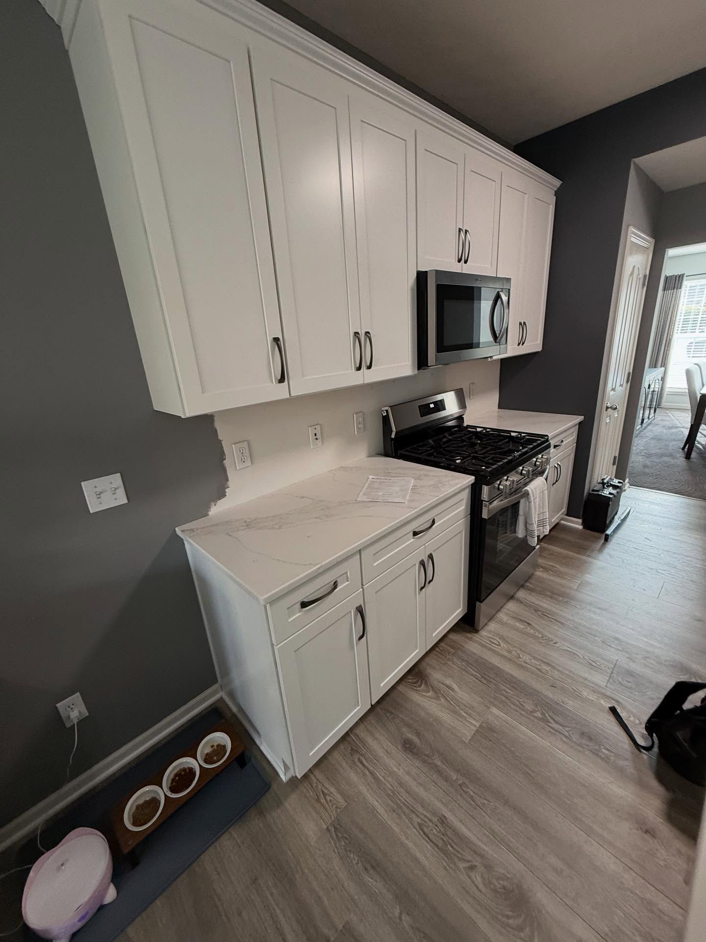 Bright kitchen with white cabinets, dark gray walls, stainless stove and microwave, and light wood flooring