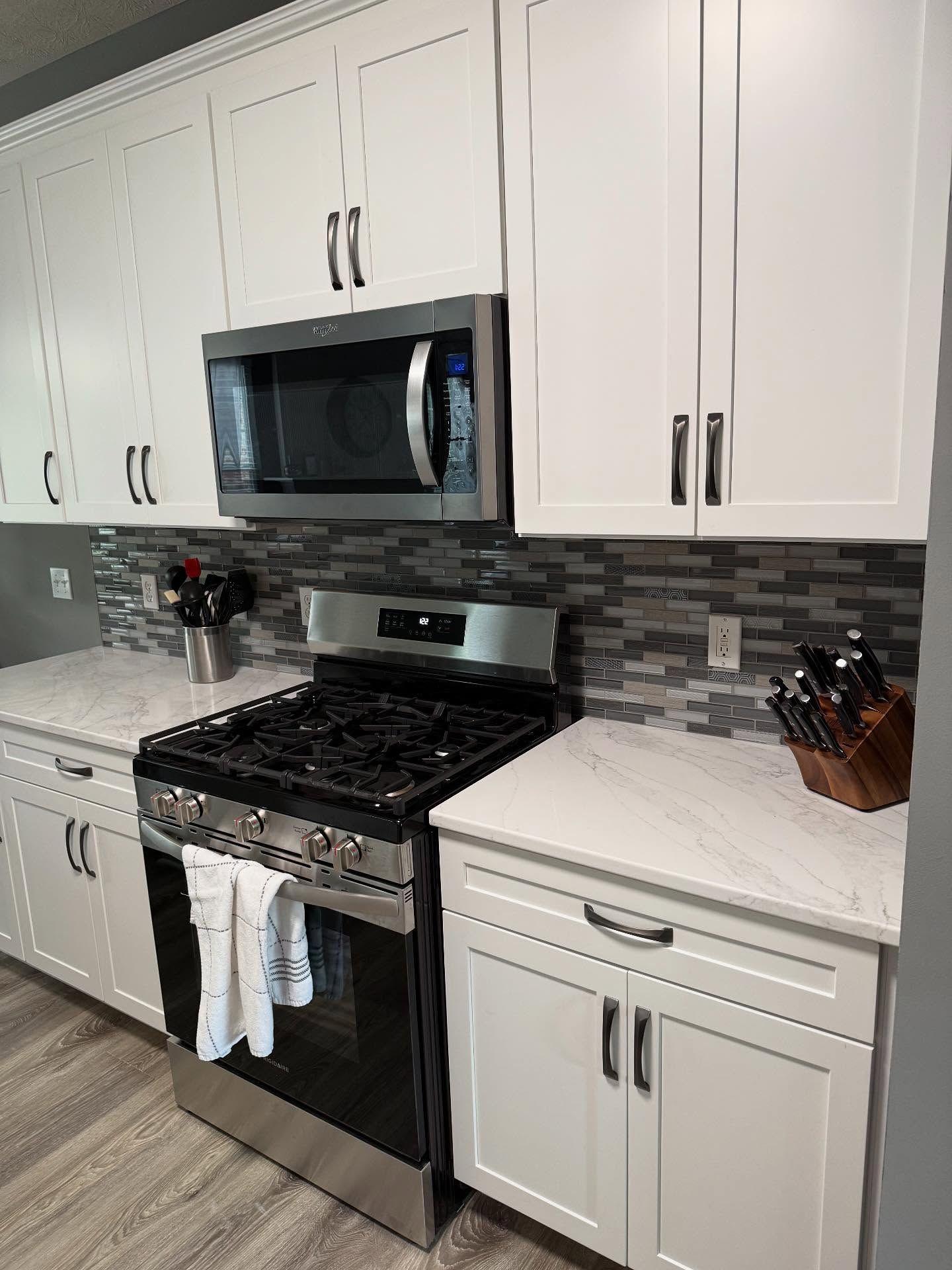 Modern kitchen with white cabinets, black stove and microwave, gray tile backsplash, and wood-look floor.