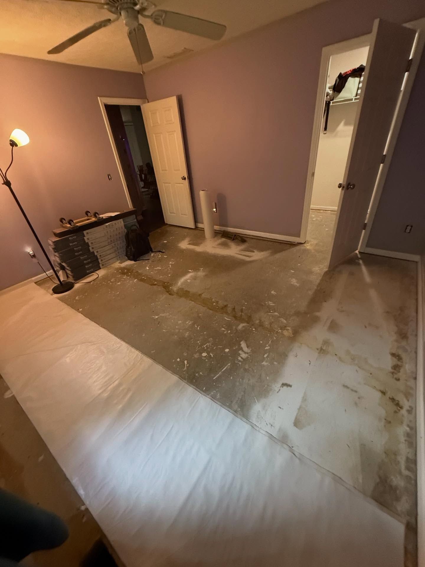 Empty bedroom with torn-up carpet, exposed floor, and a floor lamp near an open closet.