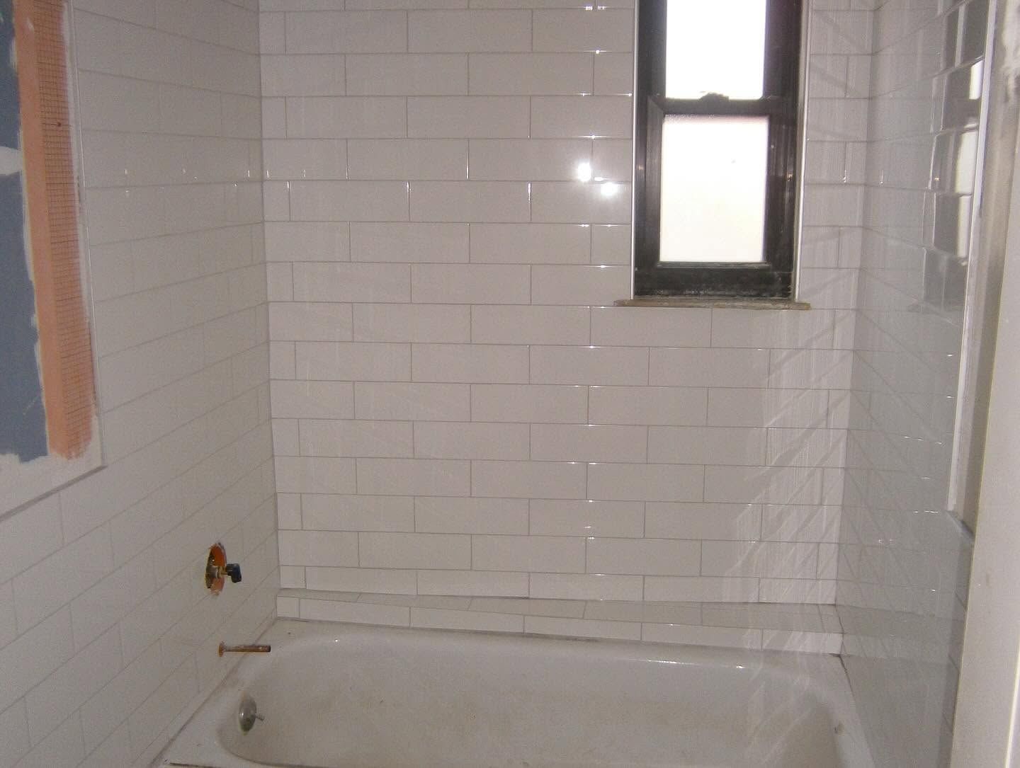 Small tiled bathroom with a white tub and a narrow window above it.