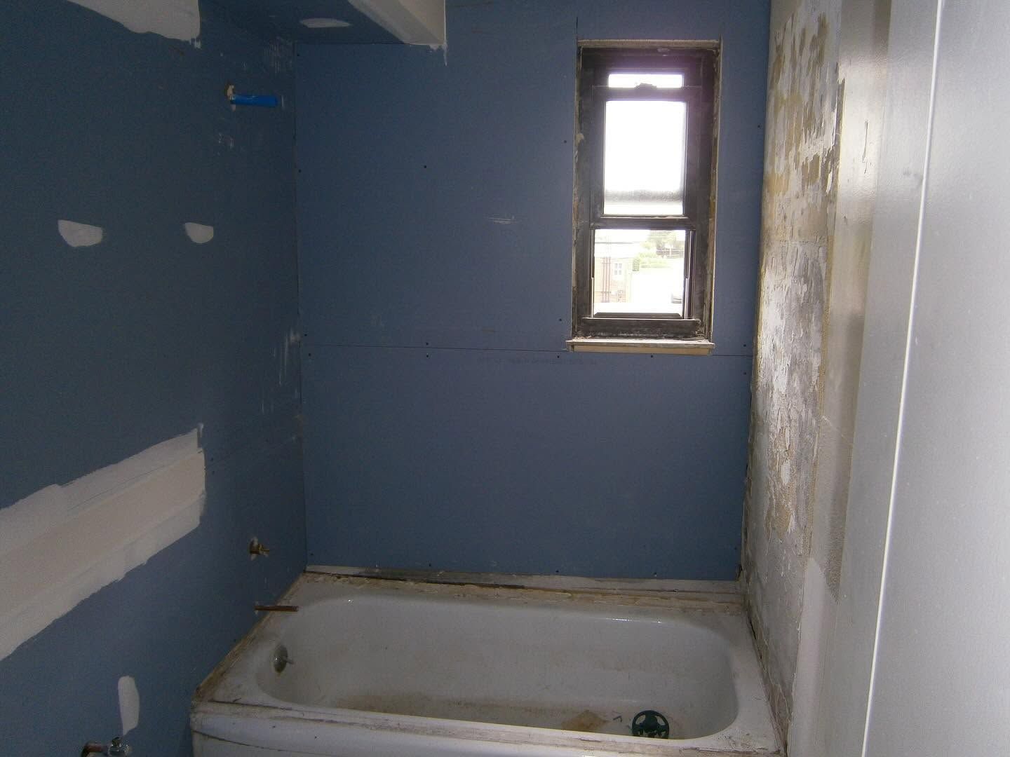 Small bathroom with blue walls, a bathtub, and a narrow window above it.