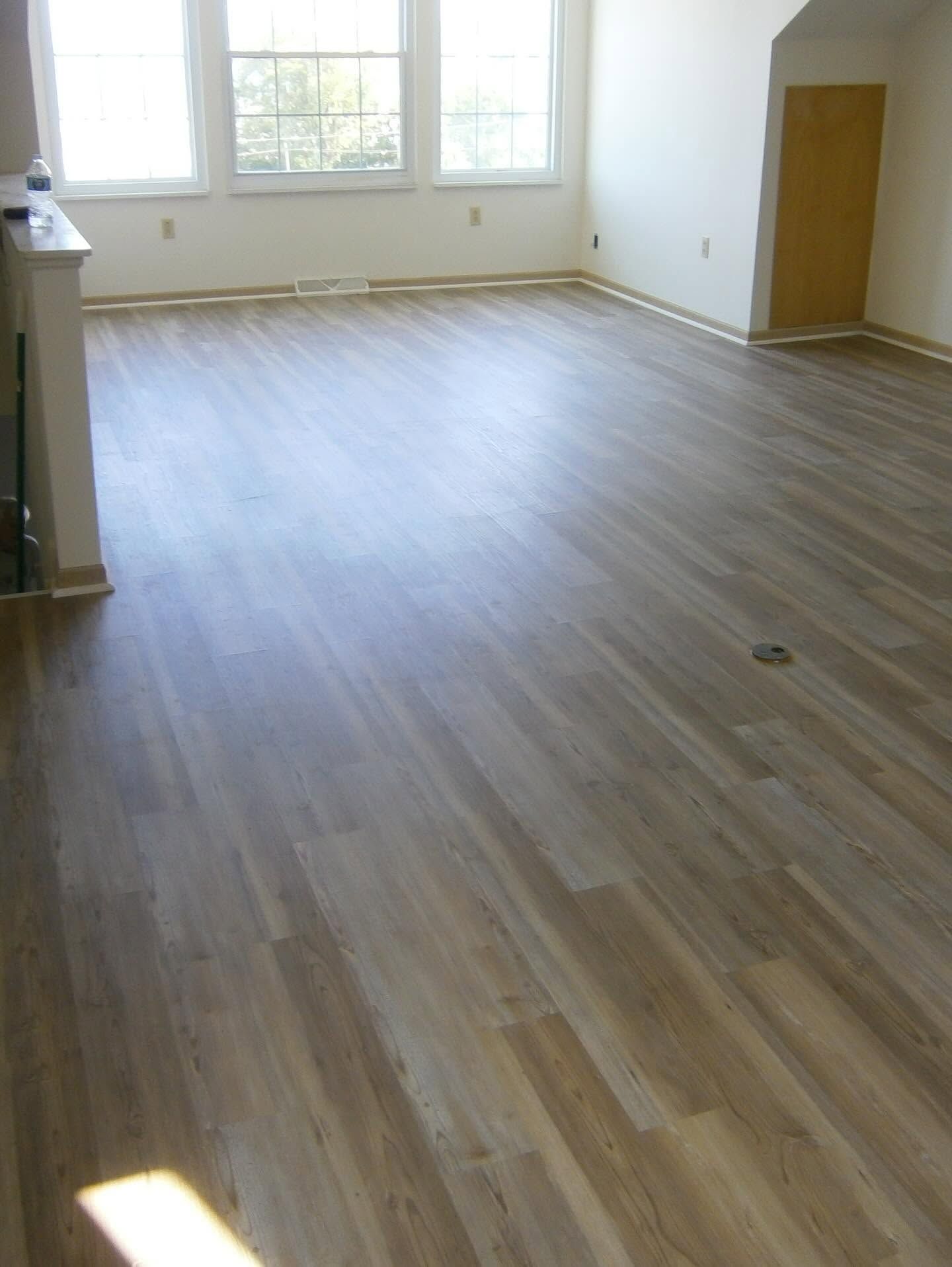 Empty room with light wood flooring, white walls, and sunlight from large windows.