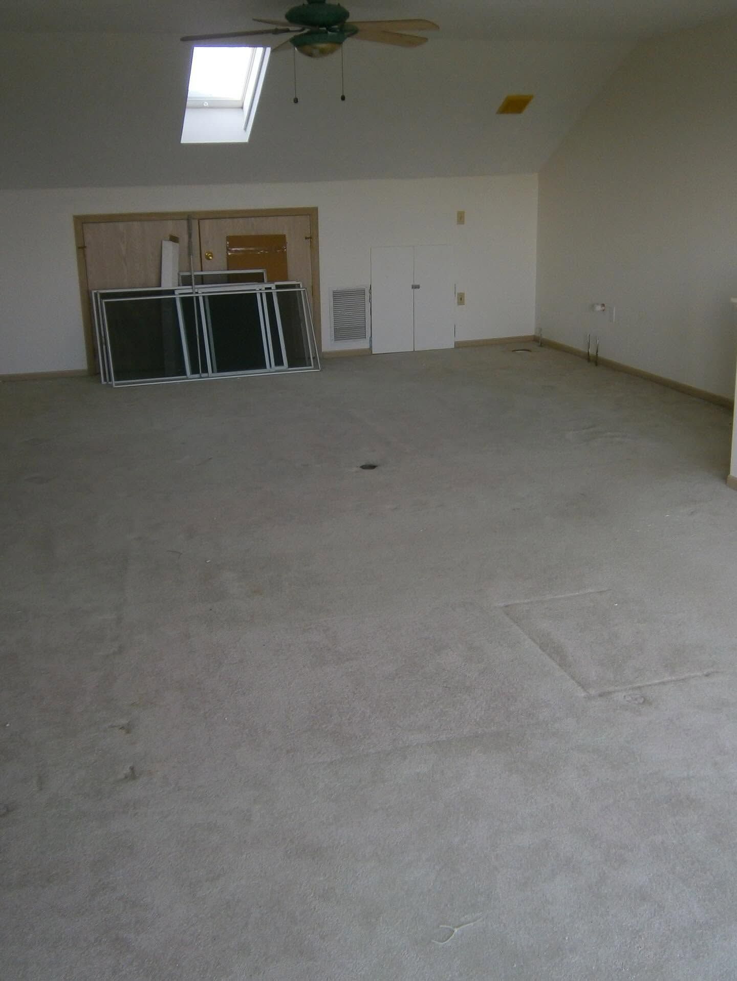 Empty room with carpet, ceiling fan, skylight, and stacked panels near the back wall.