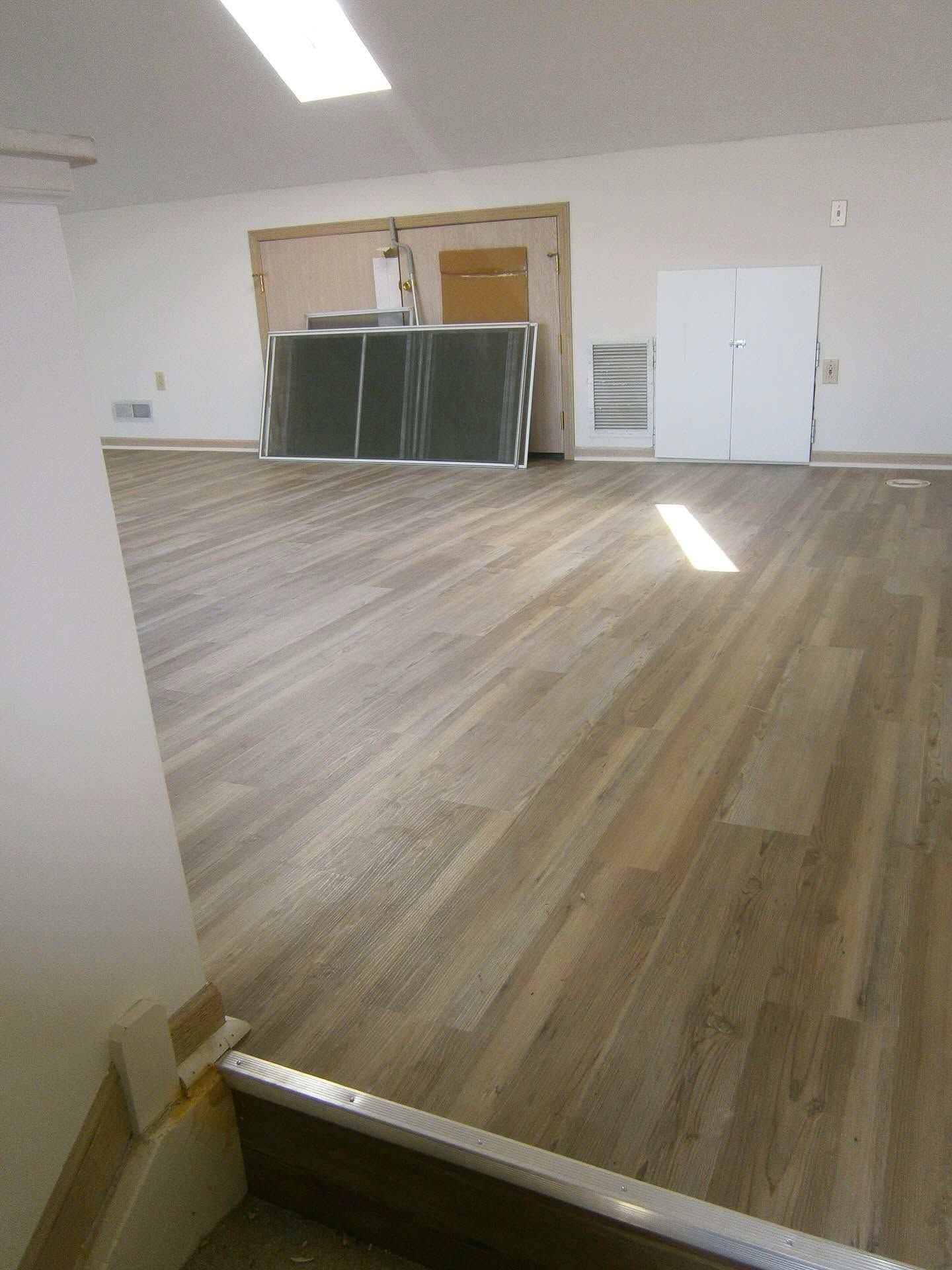 Empty room with wood-look flooring, kitchen cabinets, white door, and bright sunlight on the floor