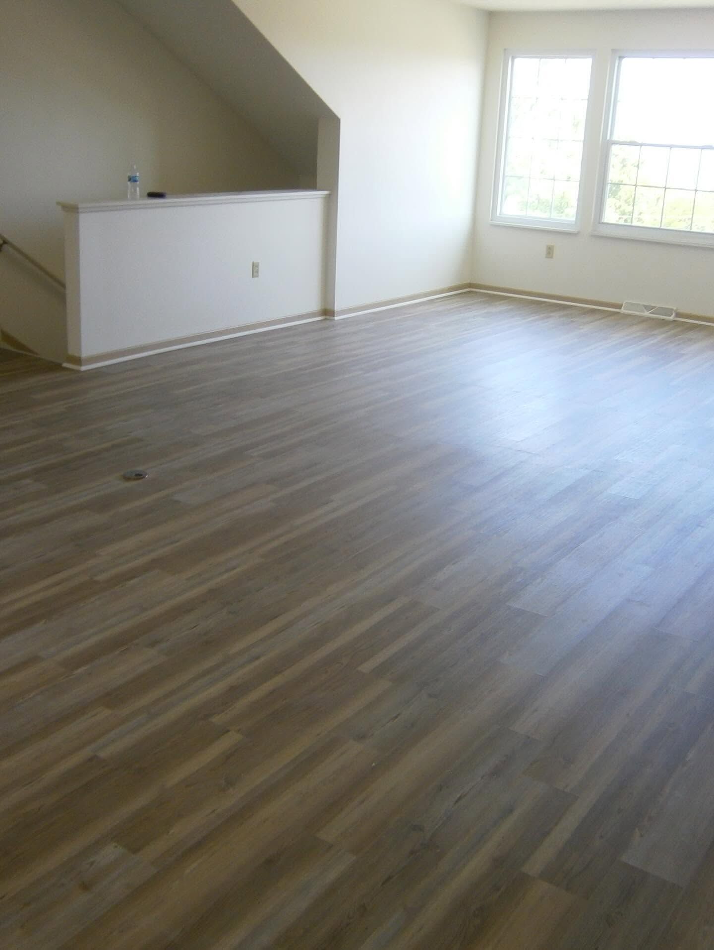 Empty room with wood flooring, white walls, staircase, and two windows.