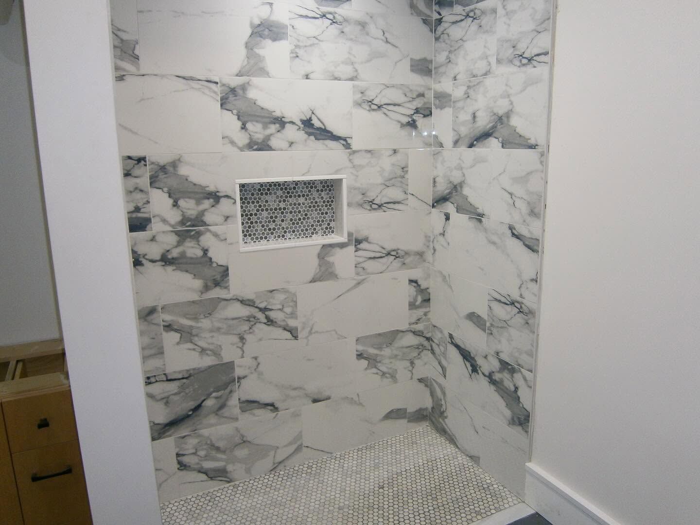 Marble-pattern shower stall with built-in niche and white mosaic floor tiles