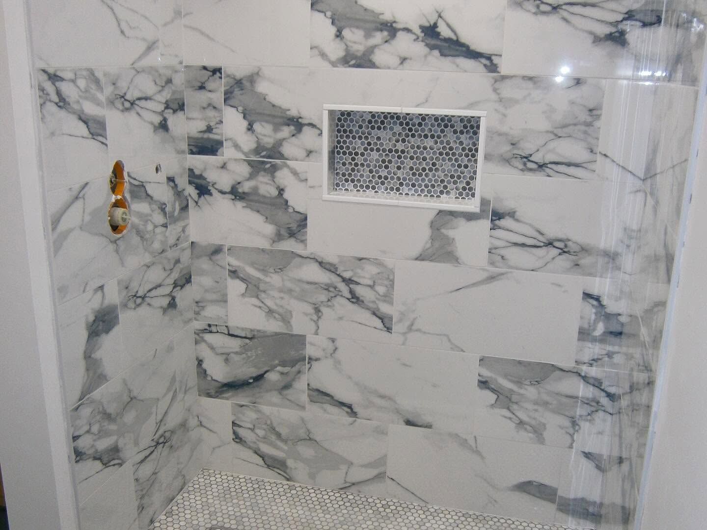 Marble-tiled shower wall with a faucet and a small rectangular vent or plaque