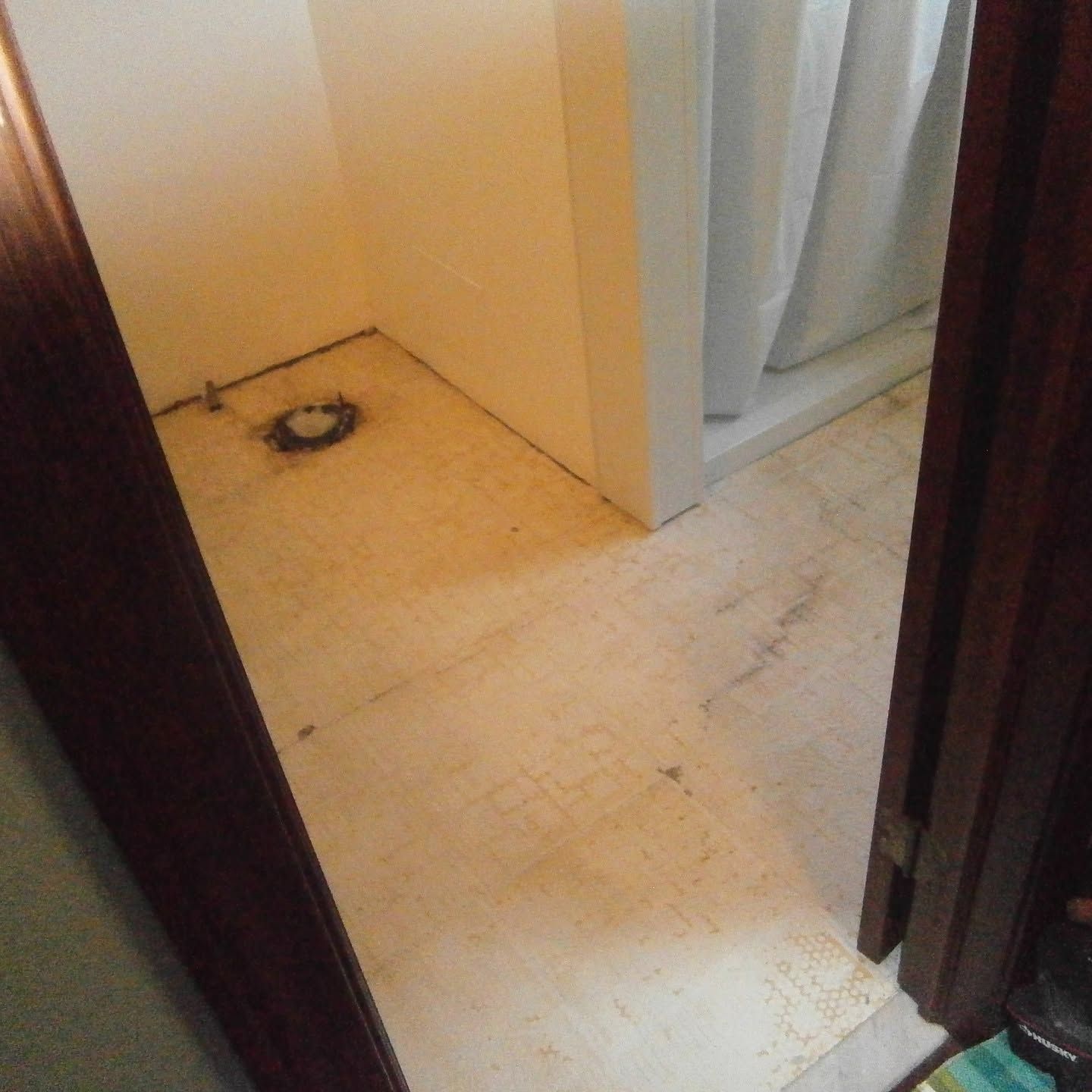 Small empty utility room with a floor drain and light-colored tile, viewed through a doorway.