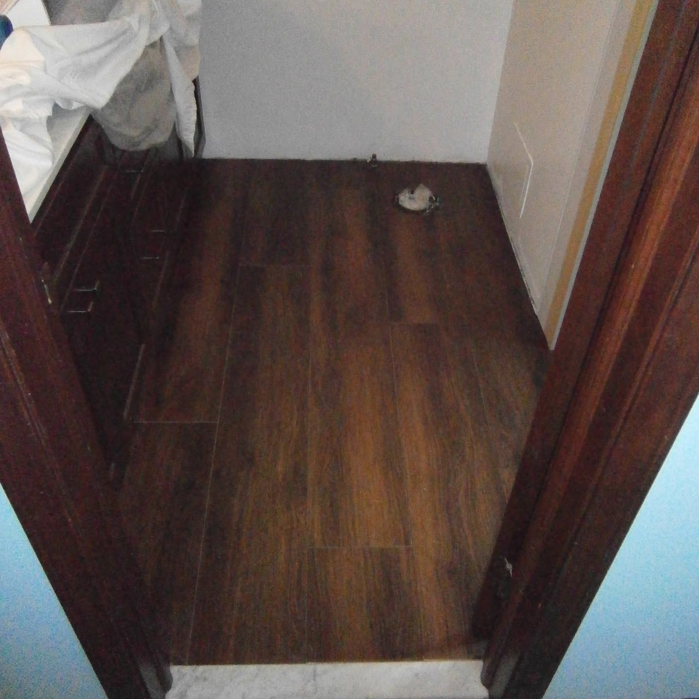 Empty dark wood-floored doorway or closet with scattered items in the corners