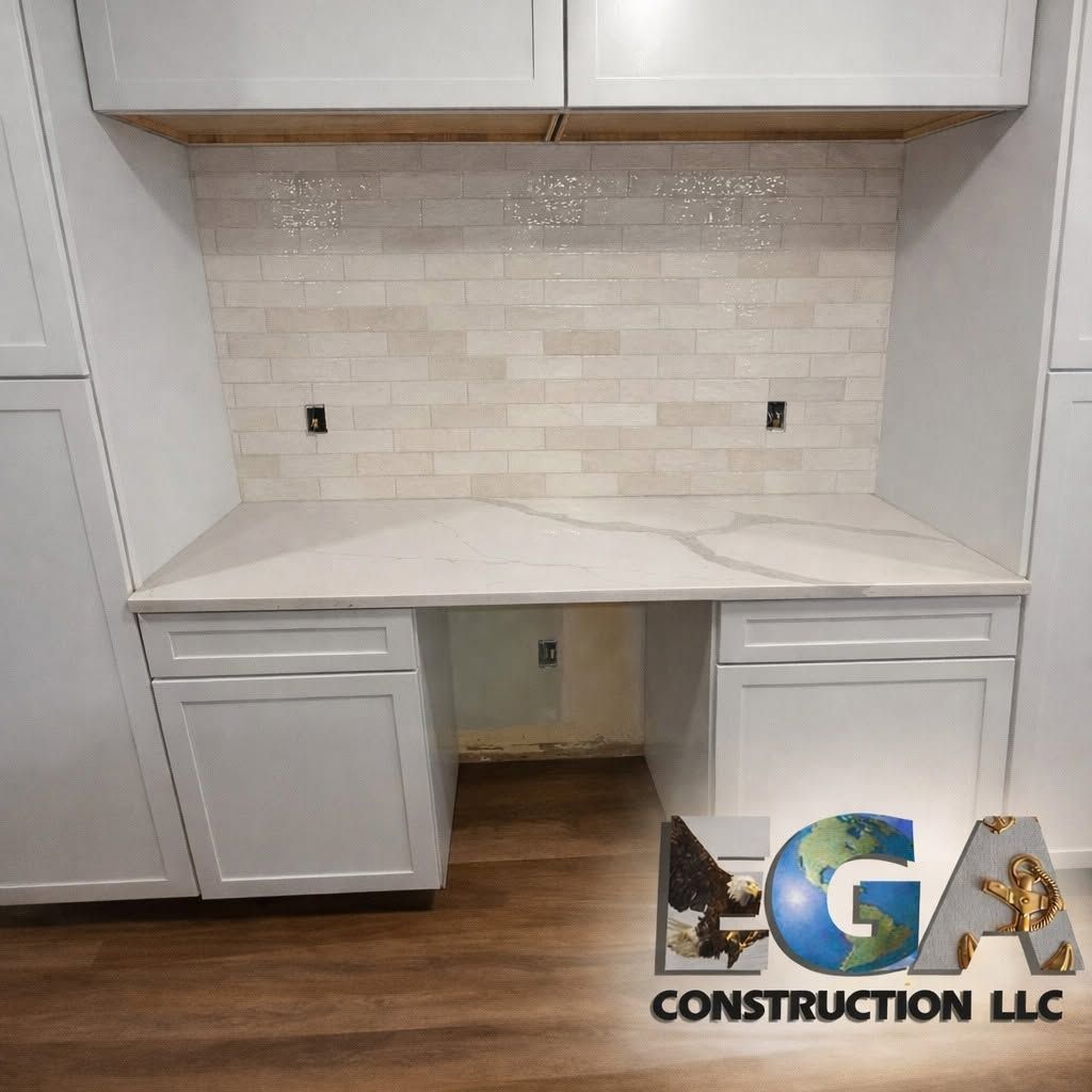 White built-in desk nook with cabinets, marble-look countertop, tile backsplash, and wood flooring.