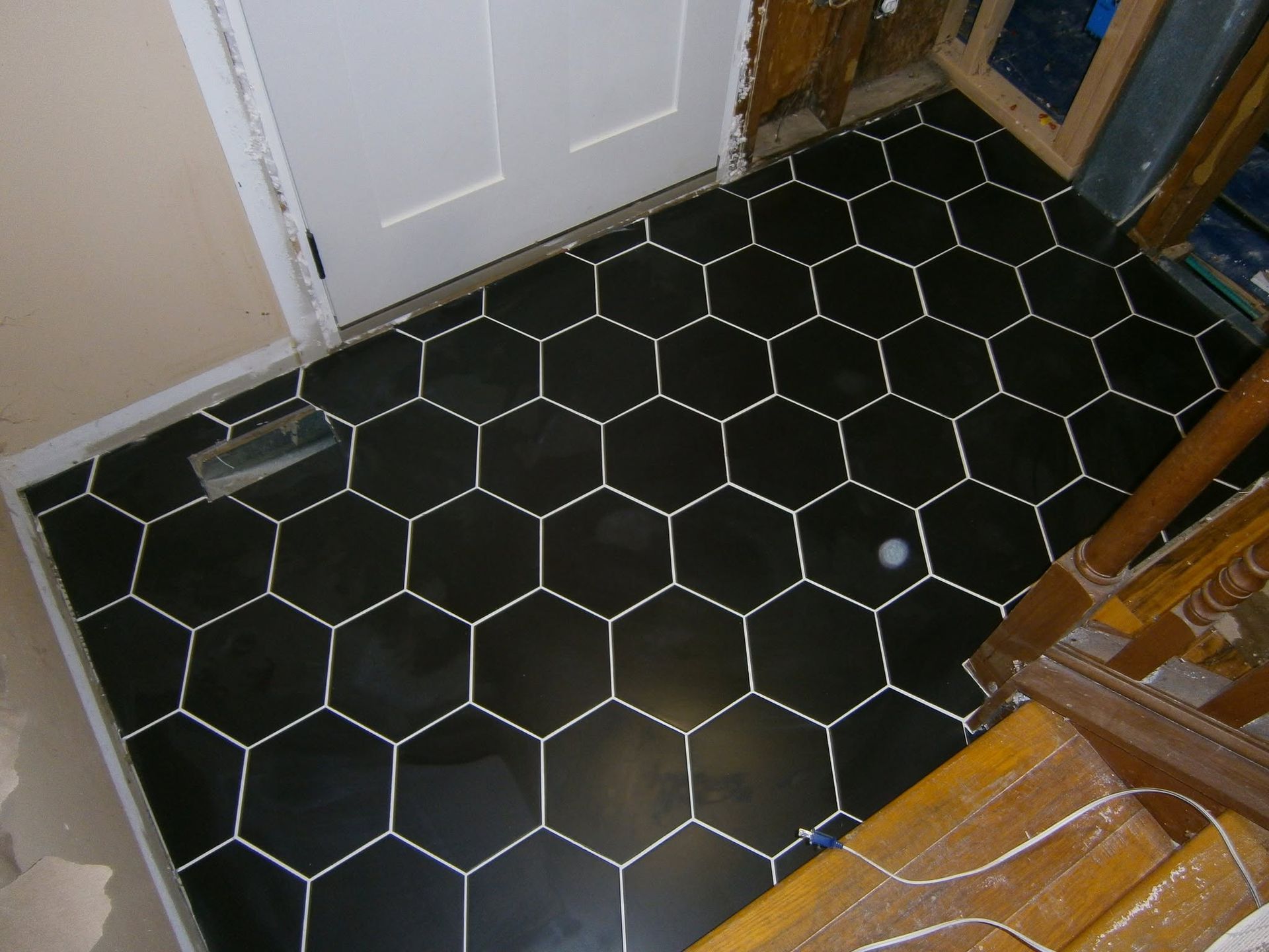 Black hexagonal tile floor near a white door and wooden stairs, with a small round drain or cap.