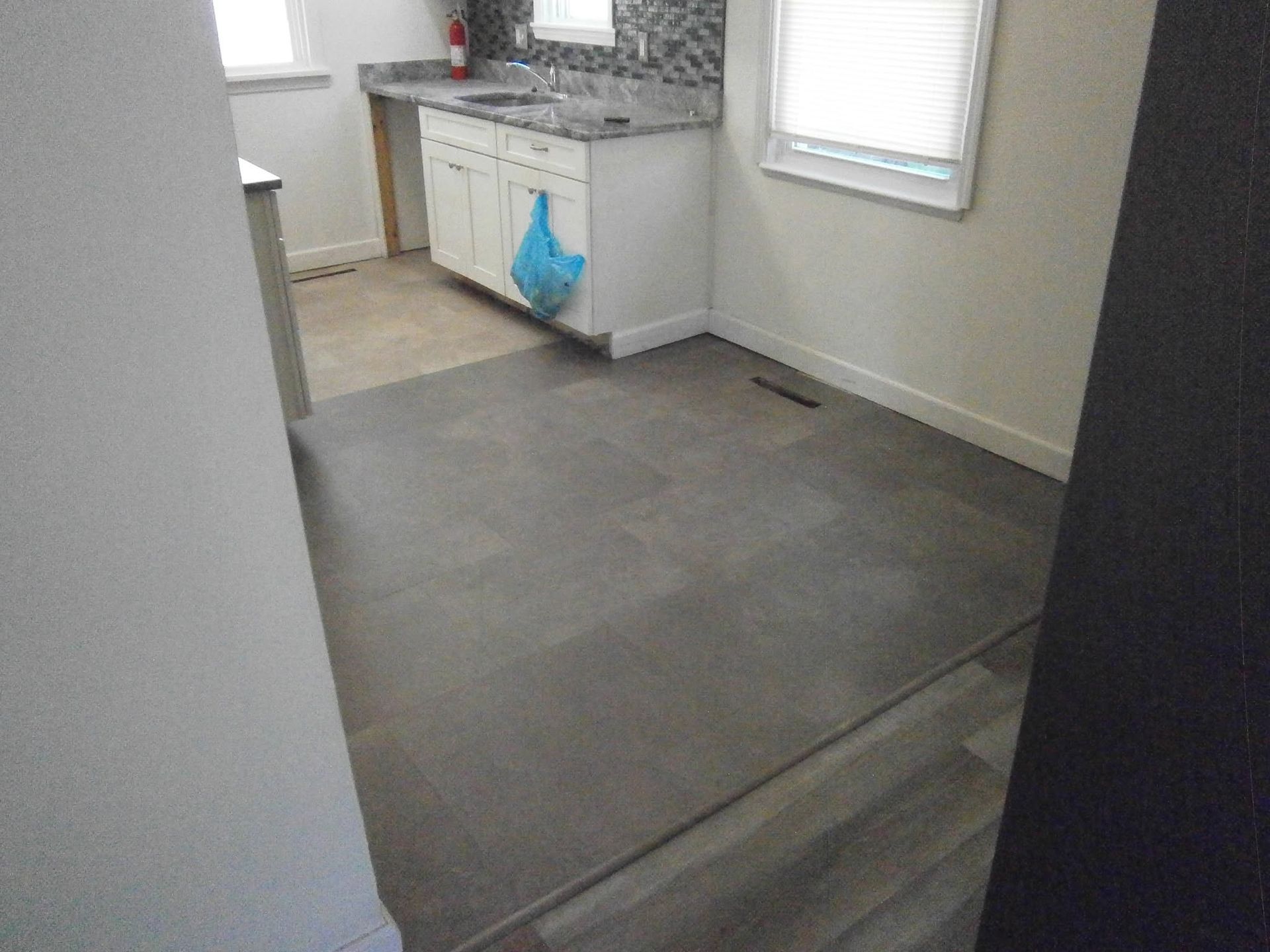 Empty room with gray carpet, white walls, and a small kitchen area in the background.