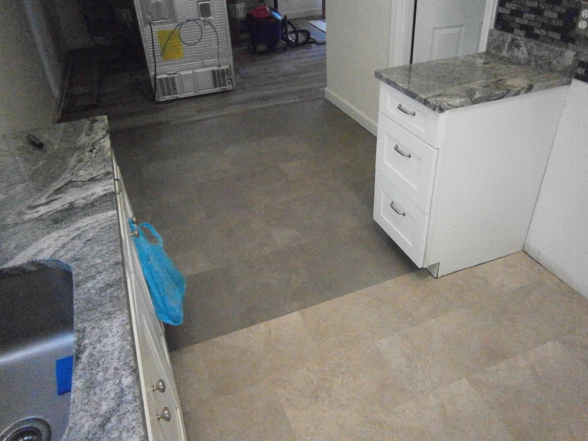 Kitchen interior with gray countertops, white cabinets, and a tiled floor leading to a doorway