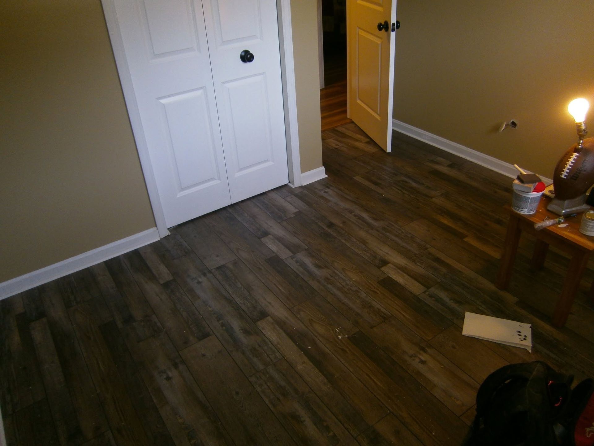 Empty room with wood flooring, white closet doors, and a lit lamp on a side table.