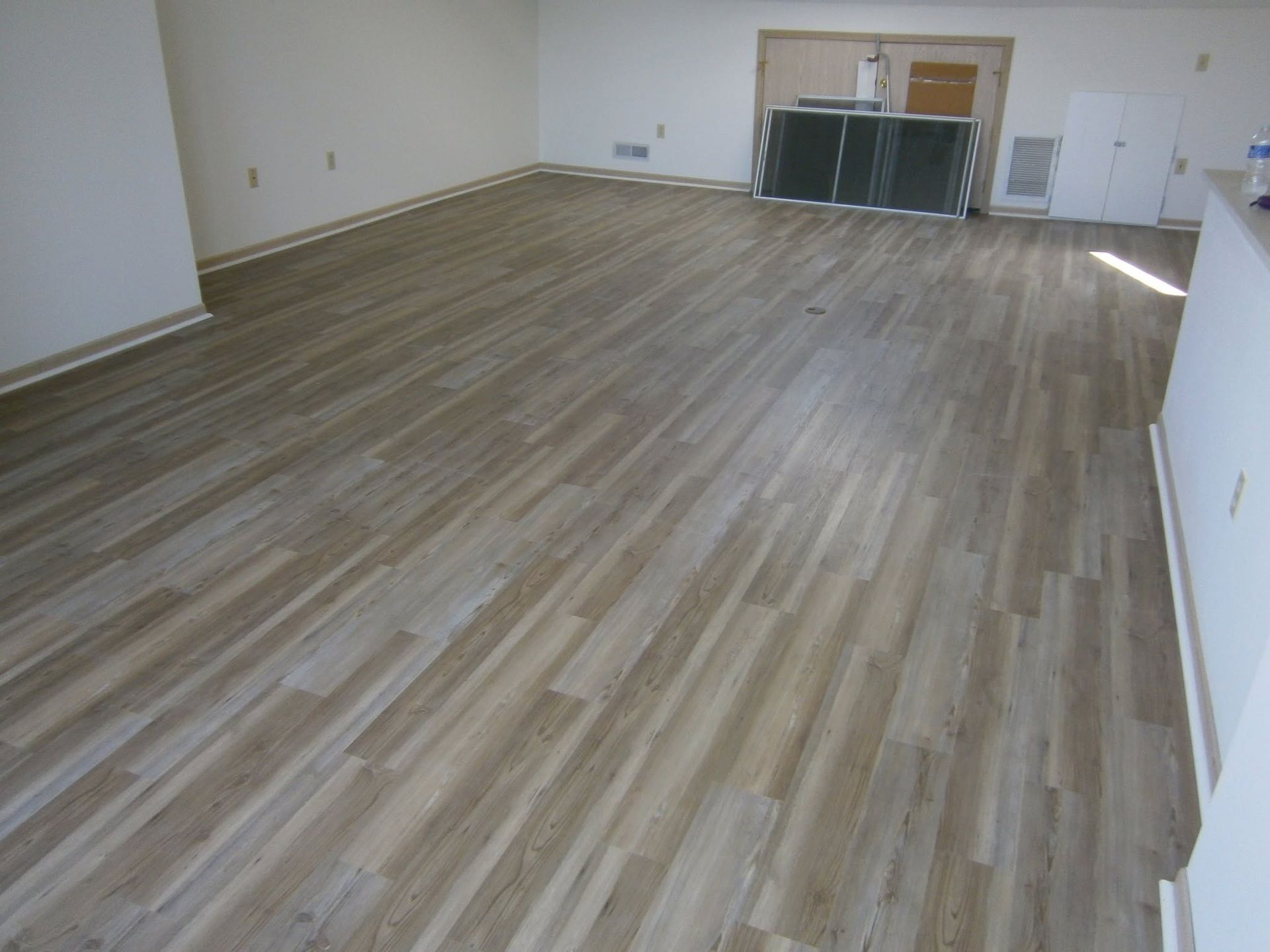 Empty room with wood flooring and a small cabinet area at the far end.