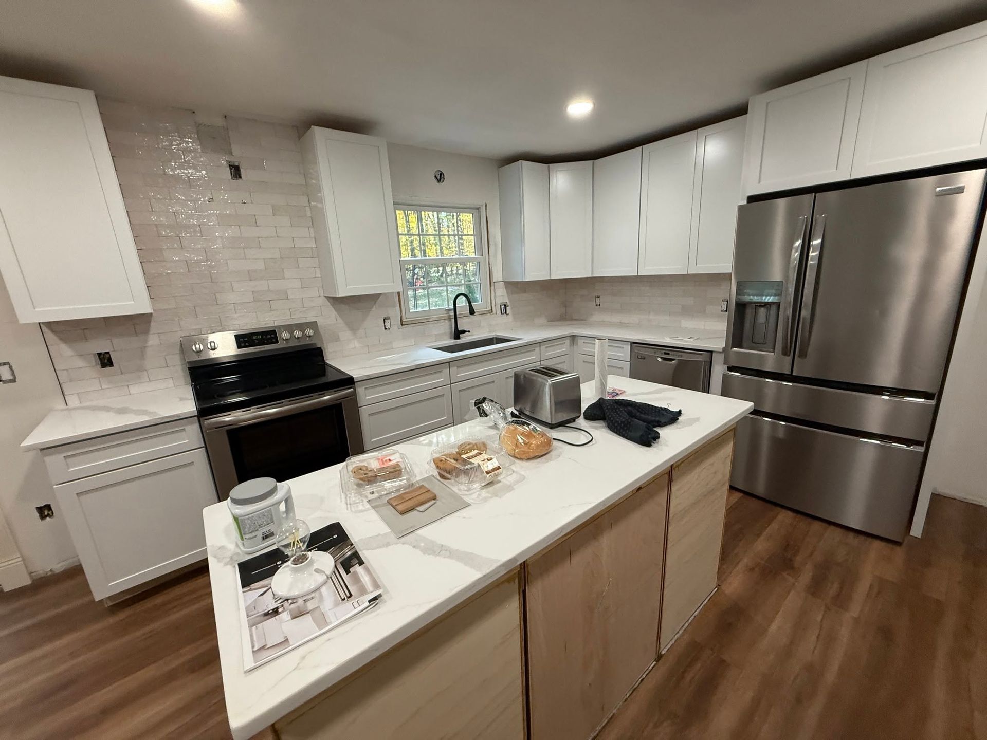 Modern white kitchen with island, stainless-steel fridge, stove, and wood floors
