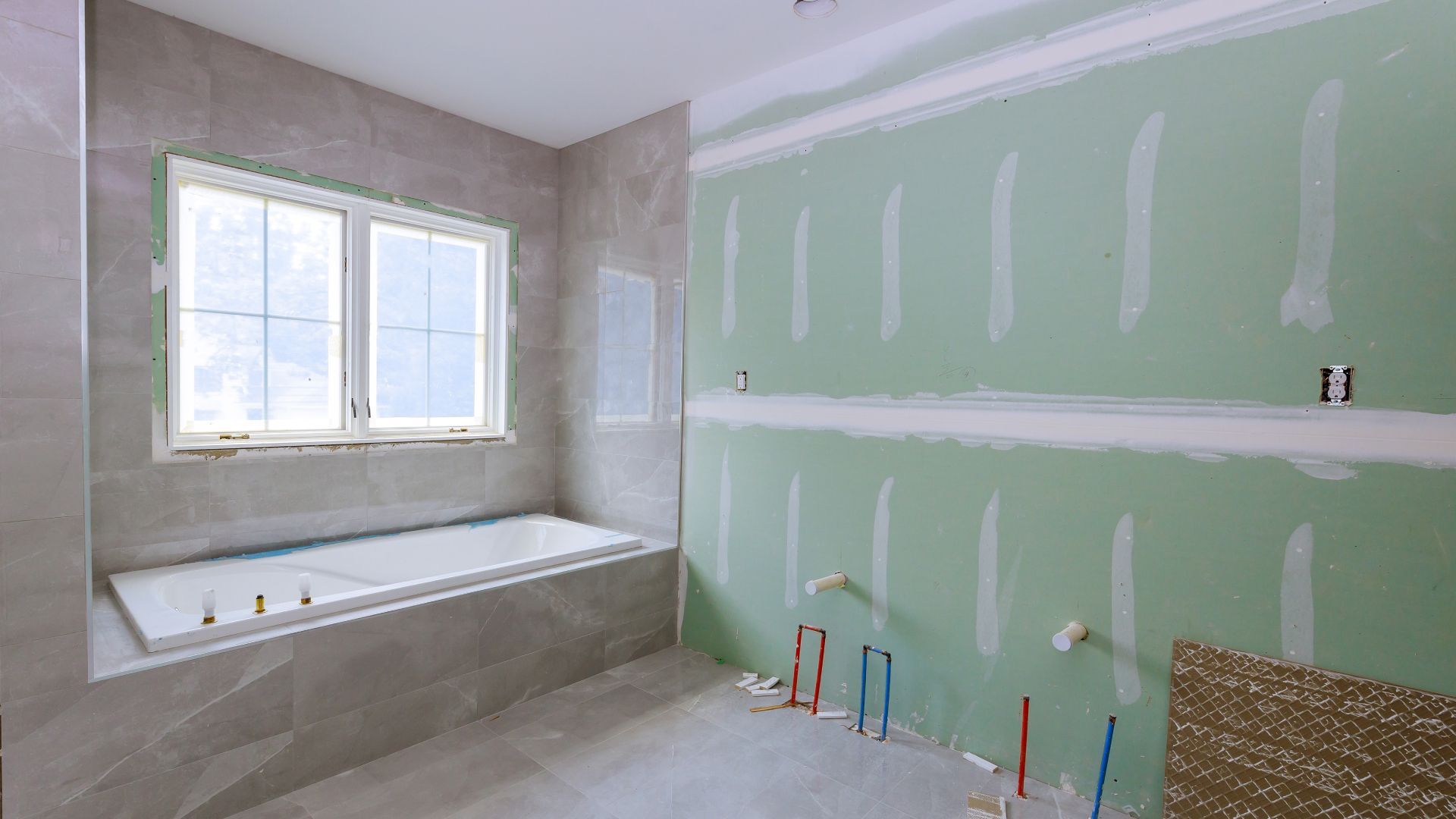 A bathroom under construction with a bathtub and two windows.