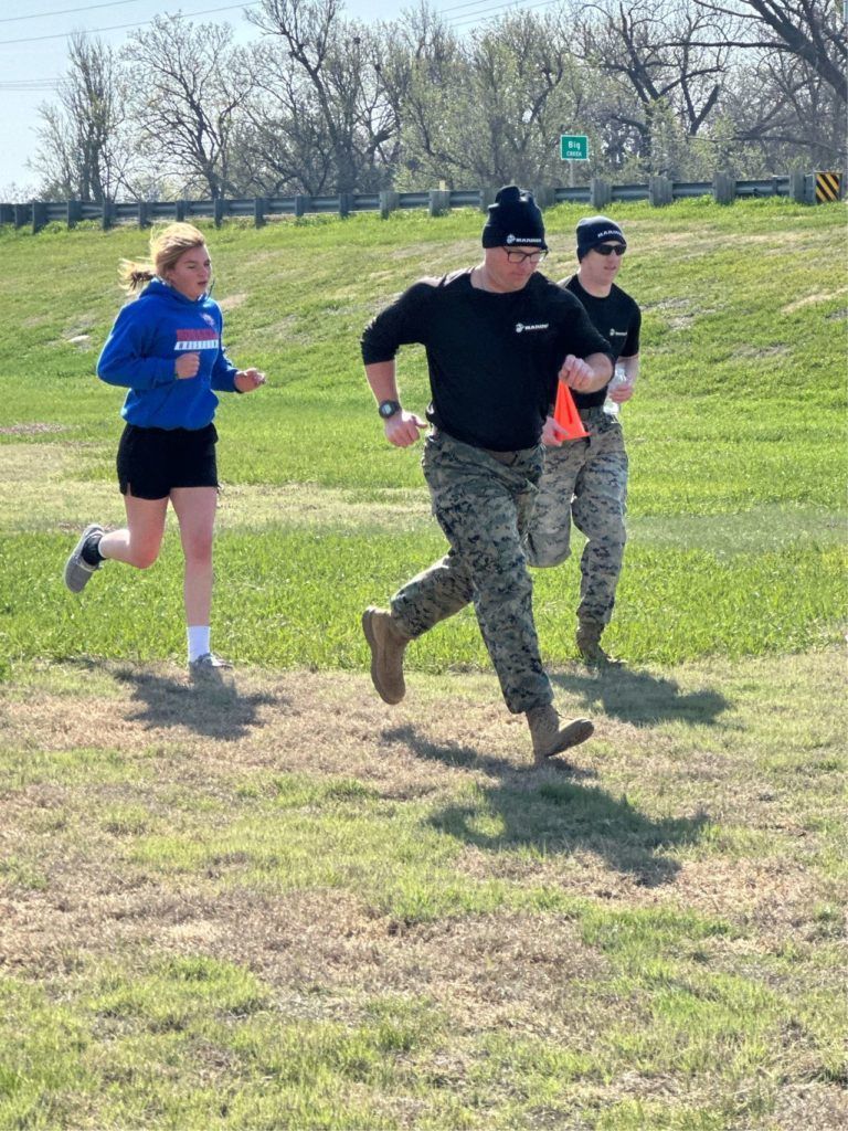 Three runners in athletic wear running on a grassy field under a bright sky