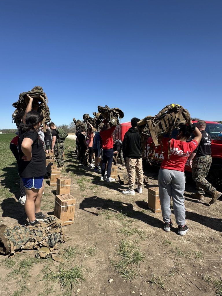 People walking in a desert field carrying bundles on their heads under a clear blue sky
