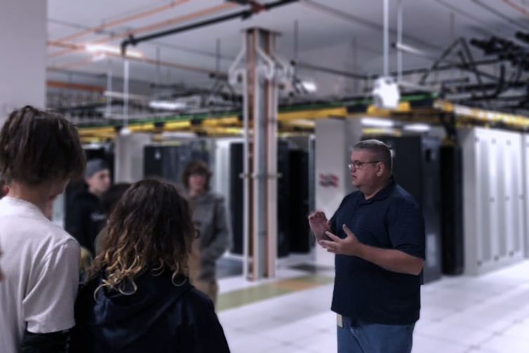 People touring a warehouse, listening to a guide holding a tablet.