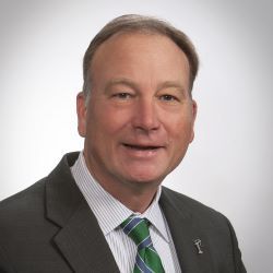 Portrait of a man in a dark suit and green striped tie against a gray background