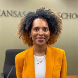 Woman in a mustard blazer smiling in an office with Kansas school signage in the background