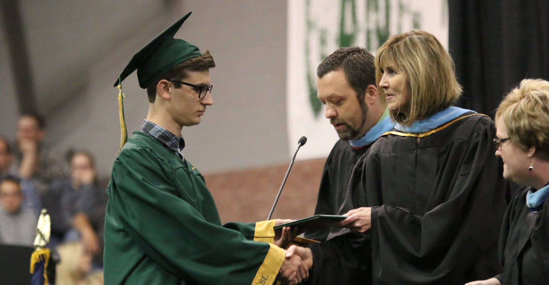 Graduate in green gown shakes hands on stage during a commencement ceremony