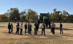 Group of people standing in a field beside a large green tractor on a sunny day