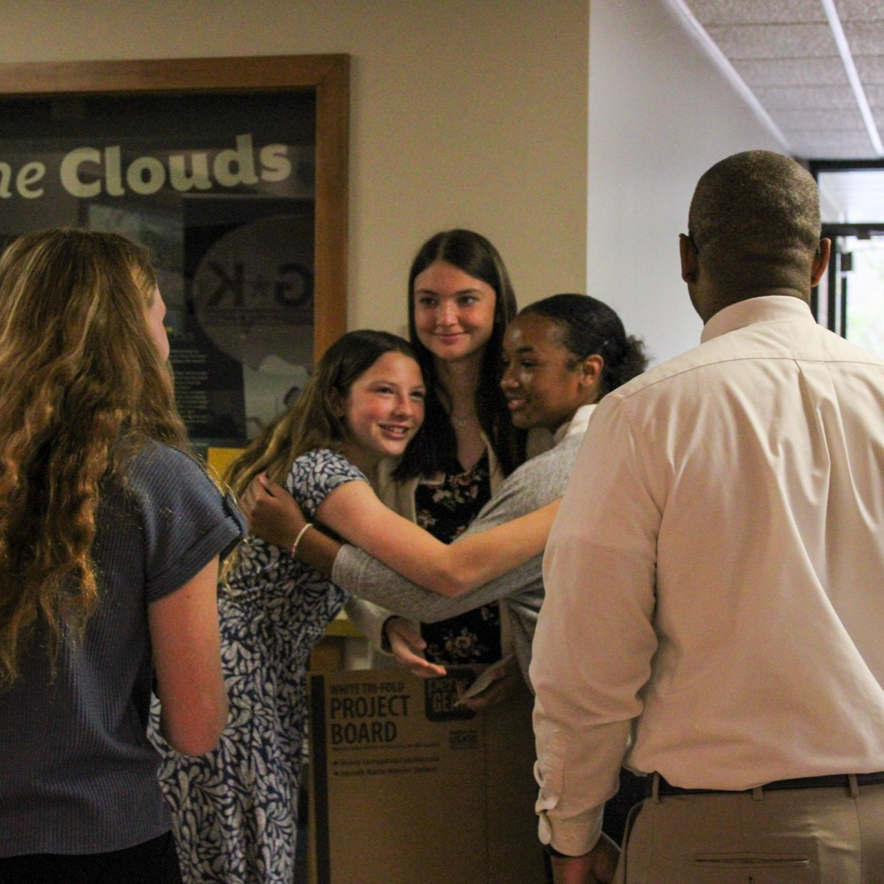 People greeting each other in a hallway, with a poster board and a sign that reads “Clouds” in the background