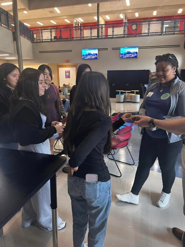 People gathered in a lobby, talking around a high table while one person holds a pink item.