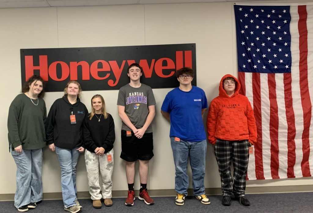 Six people standing in front of a Honeywell sign and an American flag in a hallway.