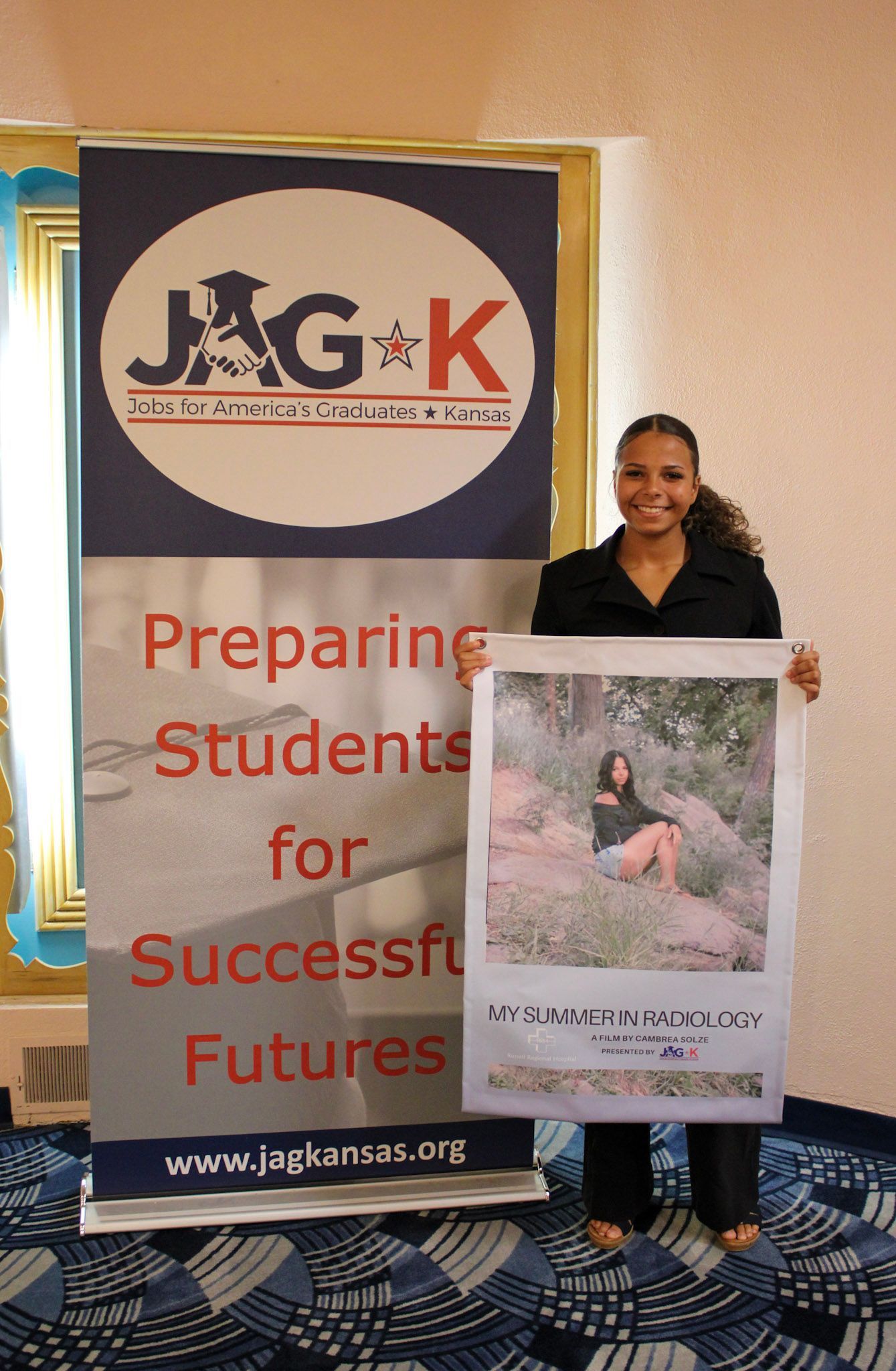 Person holding a poster beside a JGK banner reading “Preparing Students for Successful Futures.”