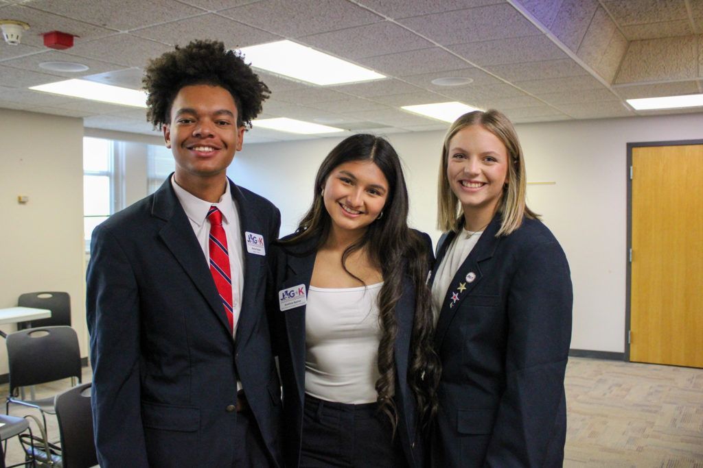 Three smiling students in business attire standing in a school hallway