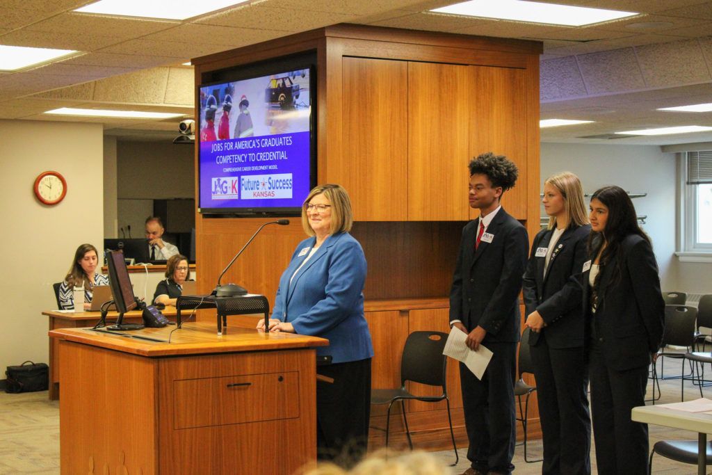 Press conference in a courthouse hallway with officials at a podium and a screen behind them.