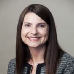 Smiling woman with long dark hair in a gray jacket against a neutral background