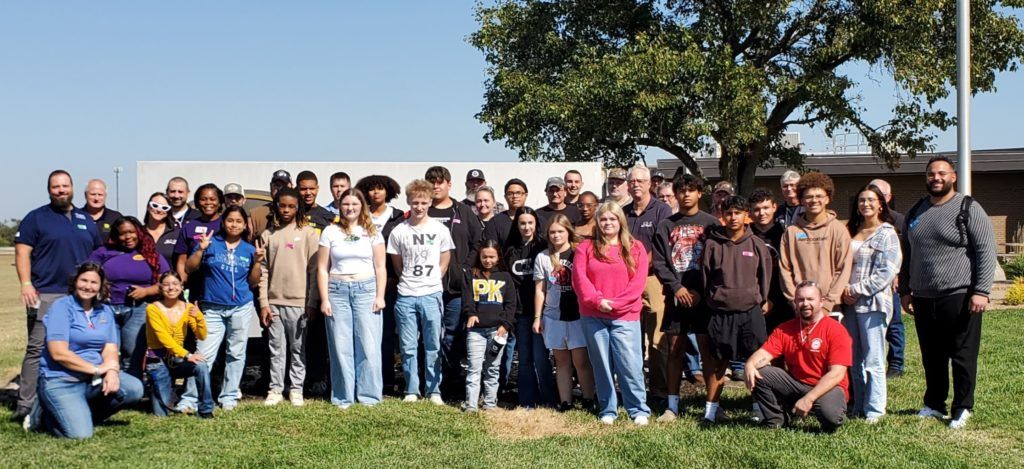 Group of people posing outdoors on a sunny day with trees and a blue sky in the background