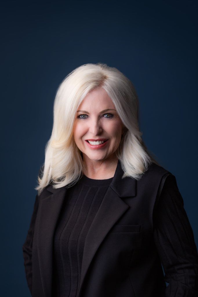 Smiling woman with silver hair in a black blazer against a dark blue background